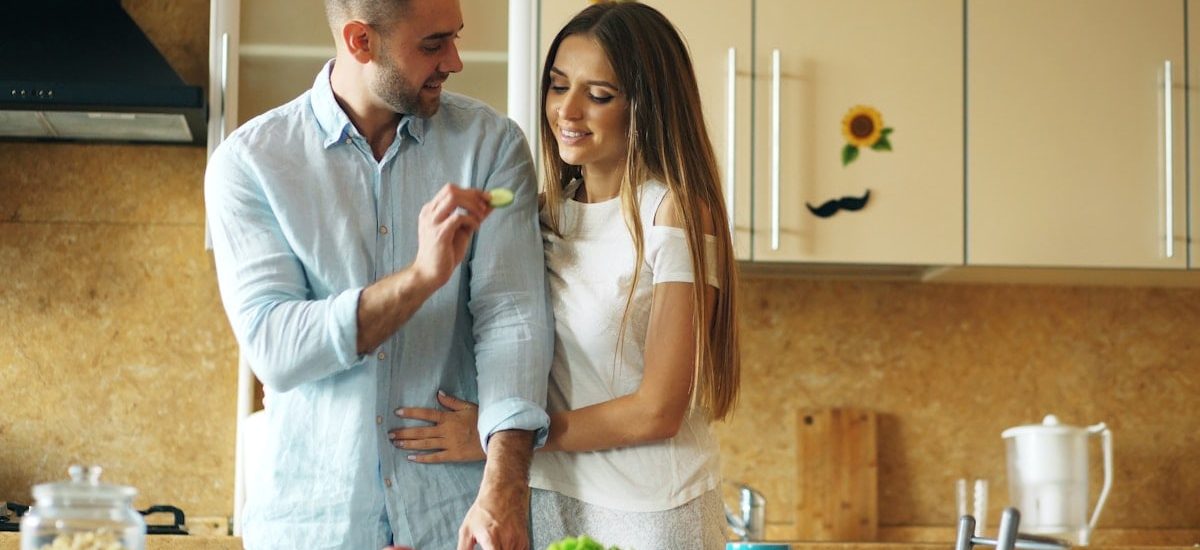 Happy young couple in the kitchen. Handsome man meet and feed his girlfriend early morning at home