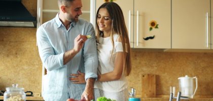 Happy young couple in the kitchen. Handsome man meet and feed his girlfriend early morning at home