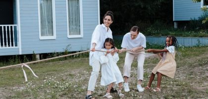 A happy family enjoys a game of tug of war in a grassy field by a house.