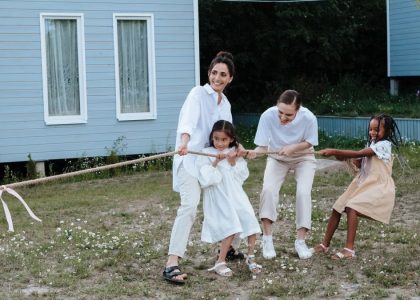 A happy family enjoys a game of tug of war in a grassy field by a house.